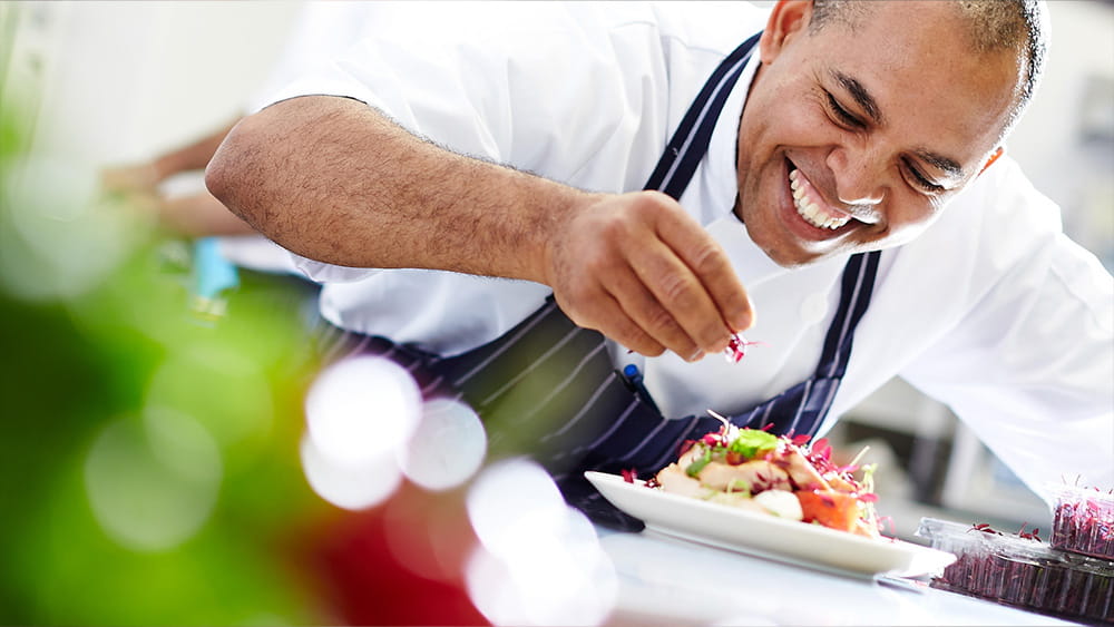 A chef sprinkles garnish on a dish